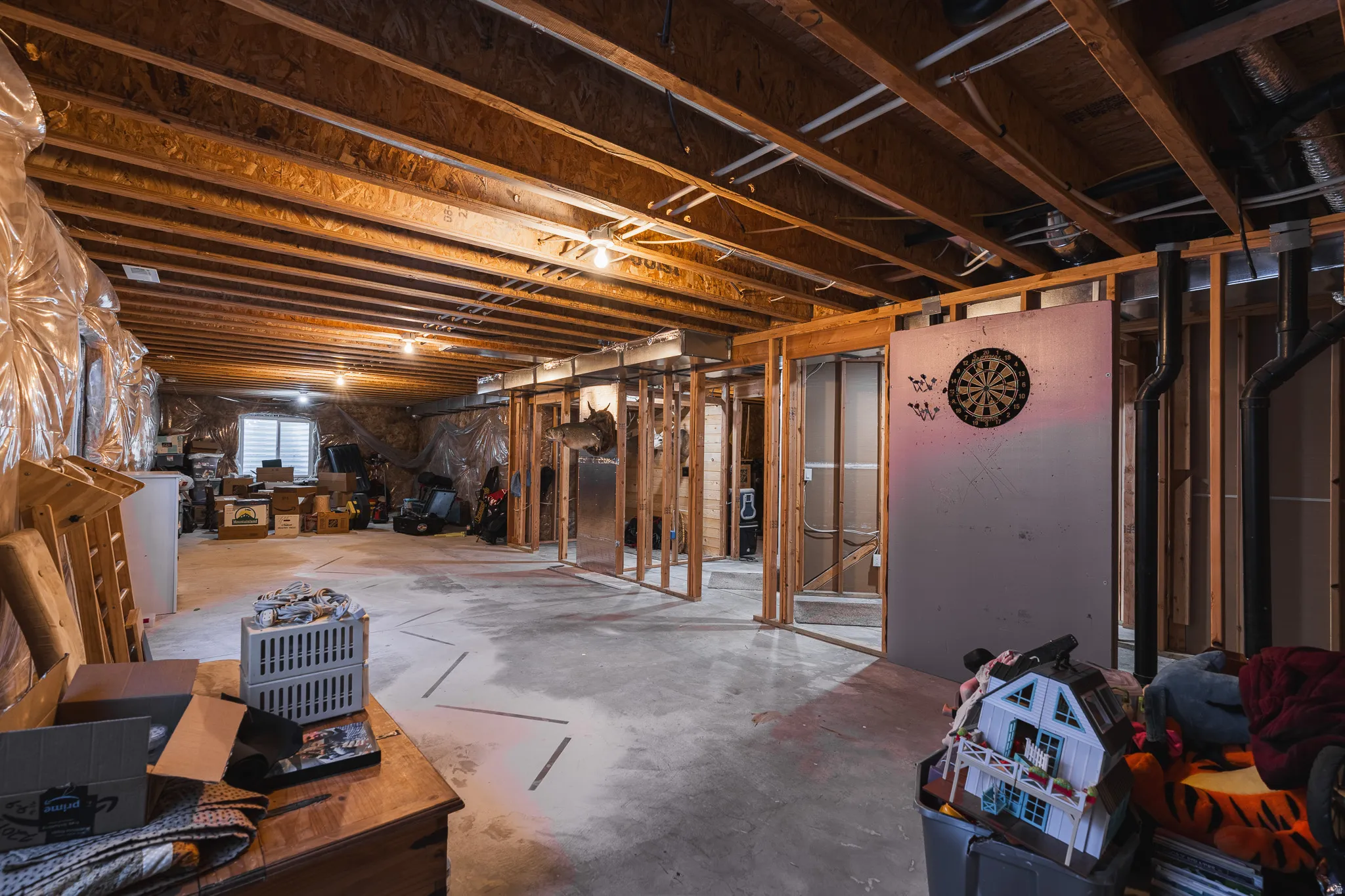 Unfinished basement with exposed wood framing, concrete flooring, and an egress window