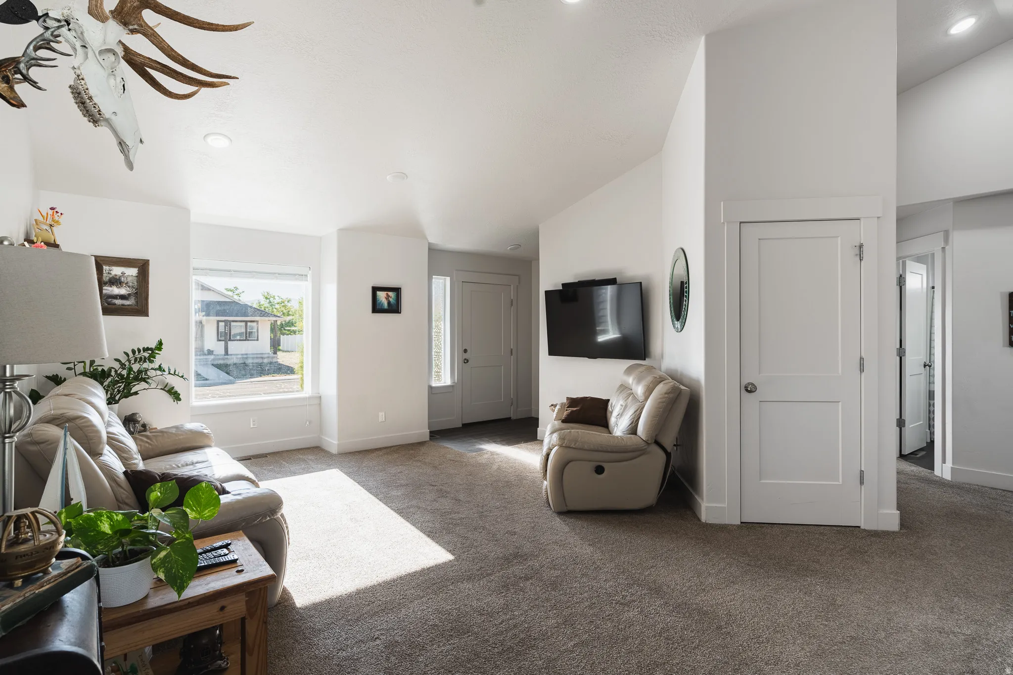 Vaulted ceilings with recessed lighting, large window with natural light, neutral carpeting, white interior doors, and a front entry door with a frosted glass insert
