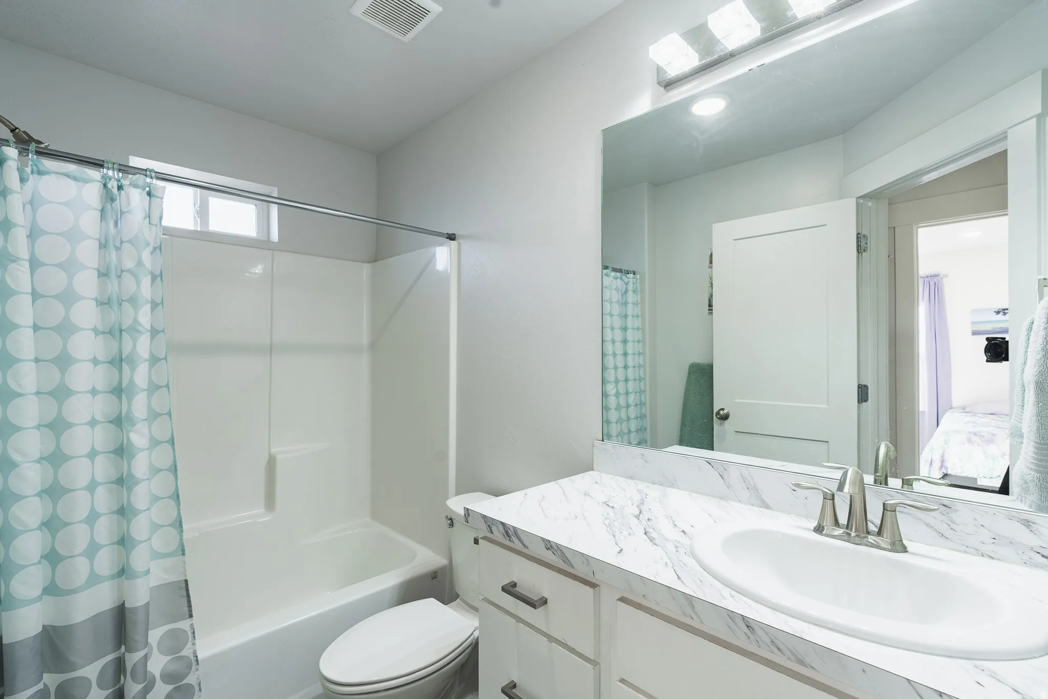 Integrated bathtub and shower combination, white vanity with an undermount sink, marbled countertop, brushed nickel faucet, and a large wall-mounted mirror