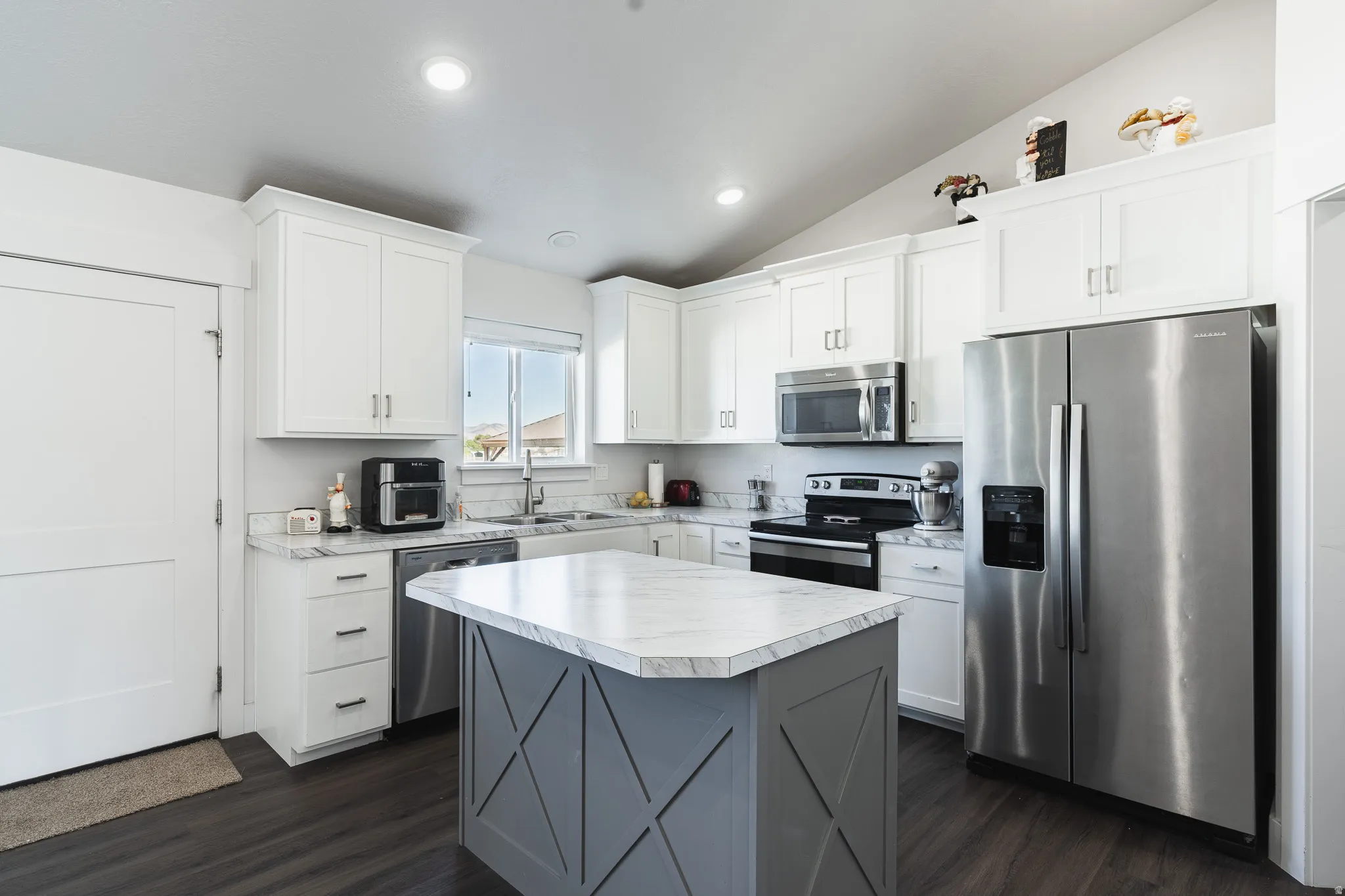 Kitchen featuring white cabinetry, stainless steel appliances, a center island with a stone-finish countertop, and wood-finish flooring