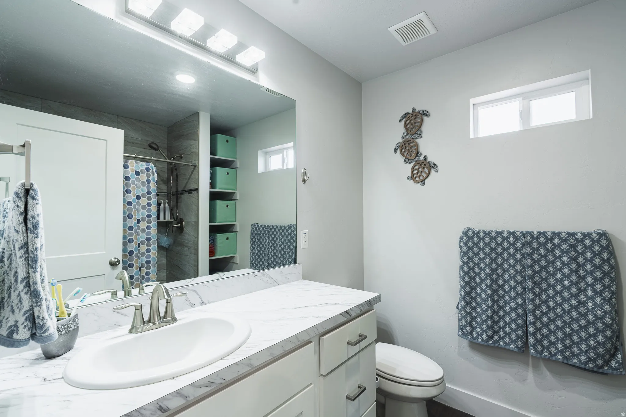 Bathroom featuring a large vanity mirror, white cabinetry with brushed nickel hardware, an undermount sink, and a light-colored countertop