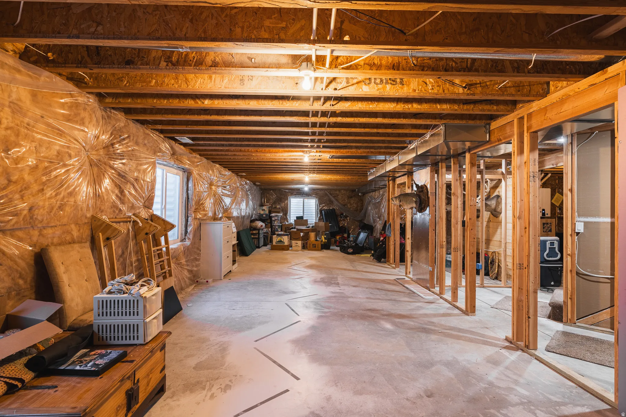 Unfinished basement with exposed wood framing, concrete flooring, and multiple windows