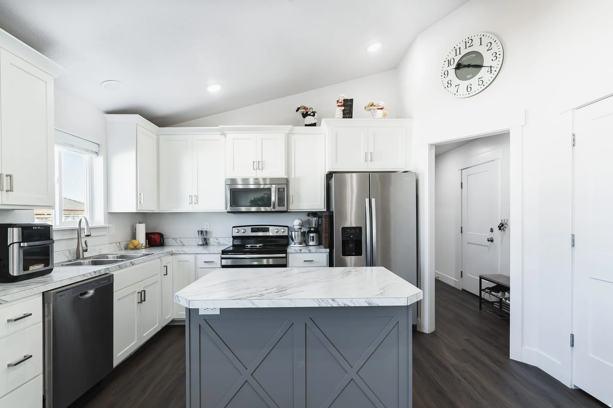 Kitchen featuring white shaker cabinetry, stainless steel appliances, marble-finish countertops, wood-finish flooring, and a central island with a decorative base