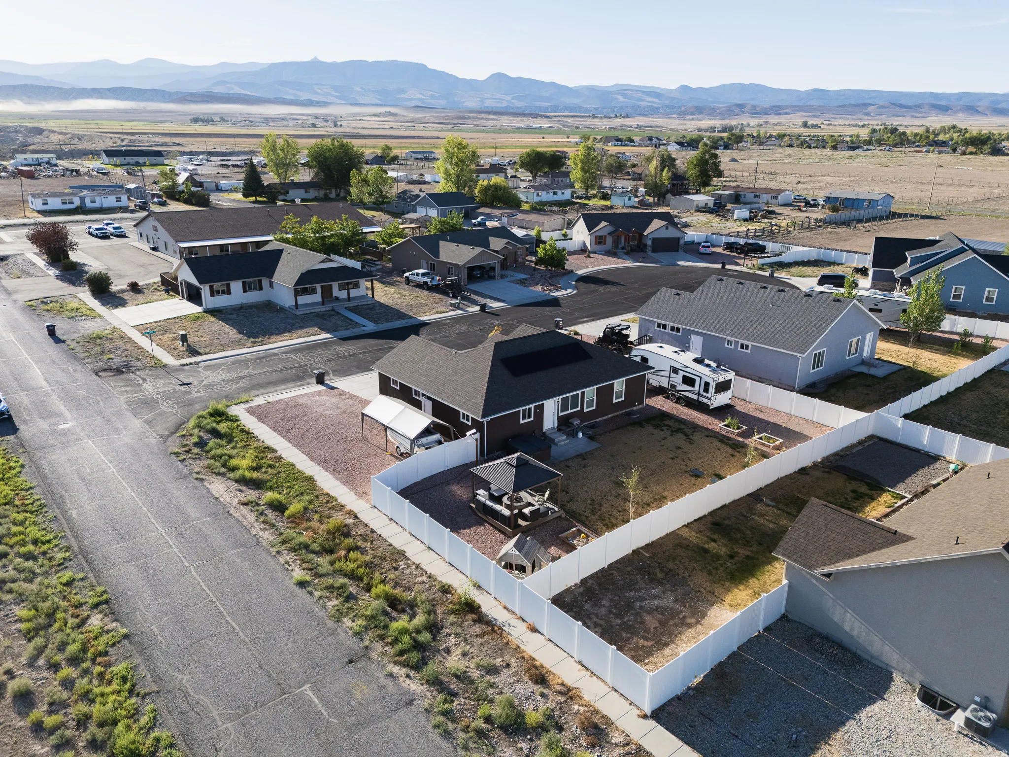 Expansive property featuring a gravel yard, white privacy fencing, and a covered patio area