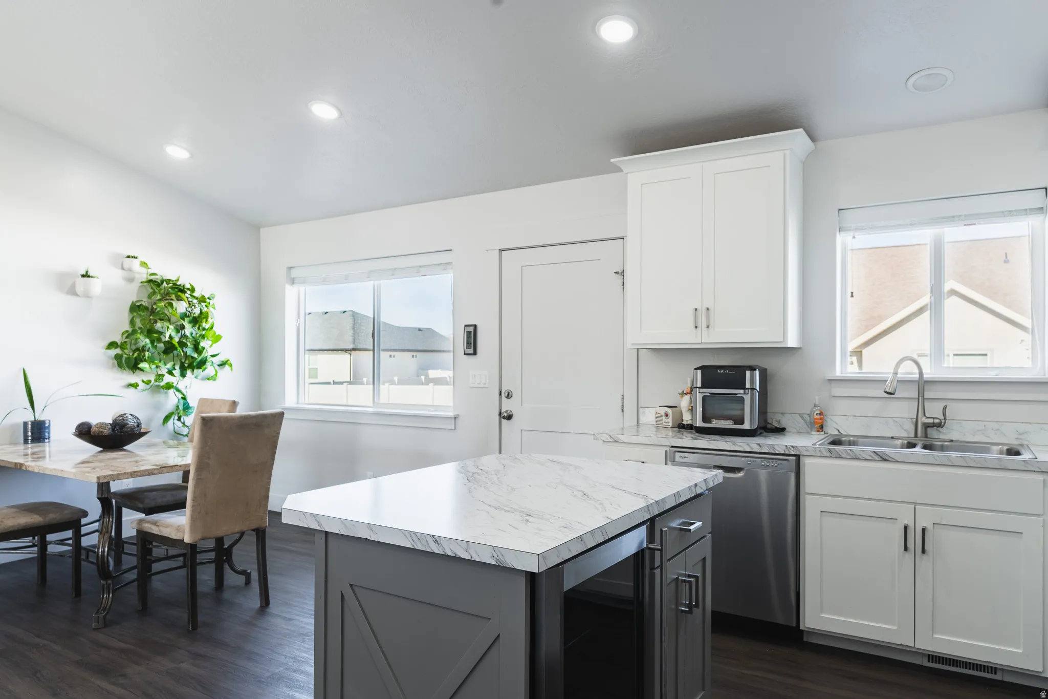 Kitchen featuring an island with a light-toned countertop, white cabinetry with silver-tone hardware, a stainless steel dishwasher, and recessed lighting