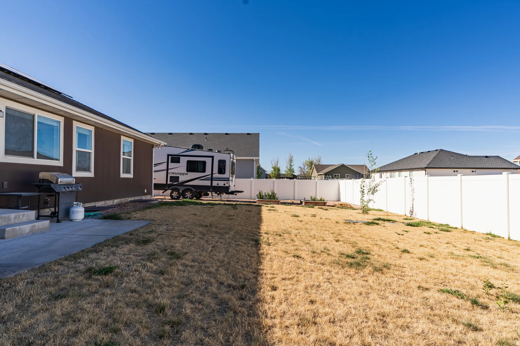 Expansive backyard featuring a concrete patio, privacy fencing, and a gravel strip