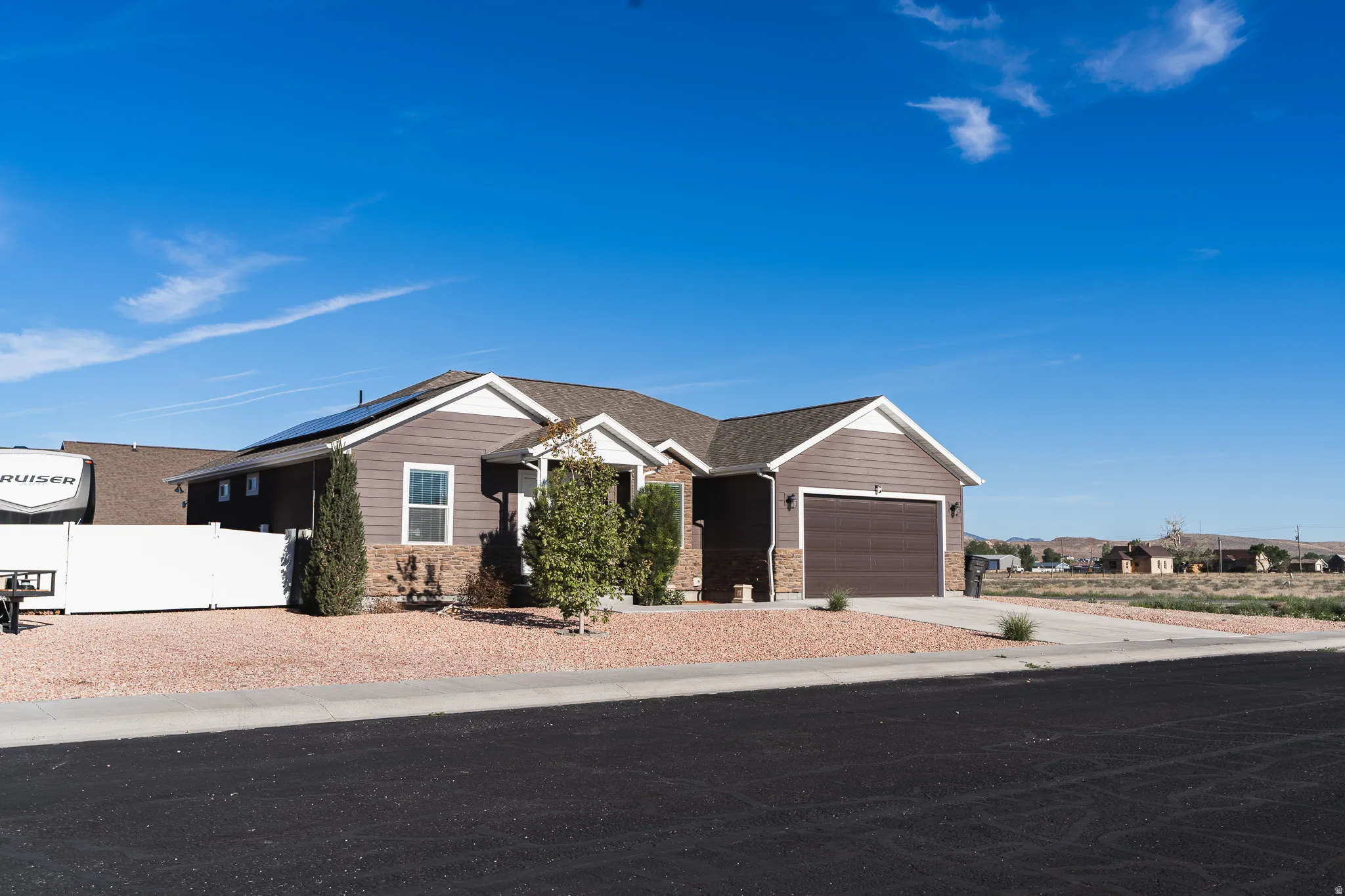 Siding exterior with stone accents, attached garage, solar panels, and a low-maintenance gravel yard