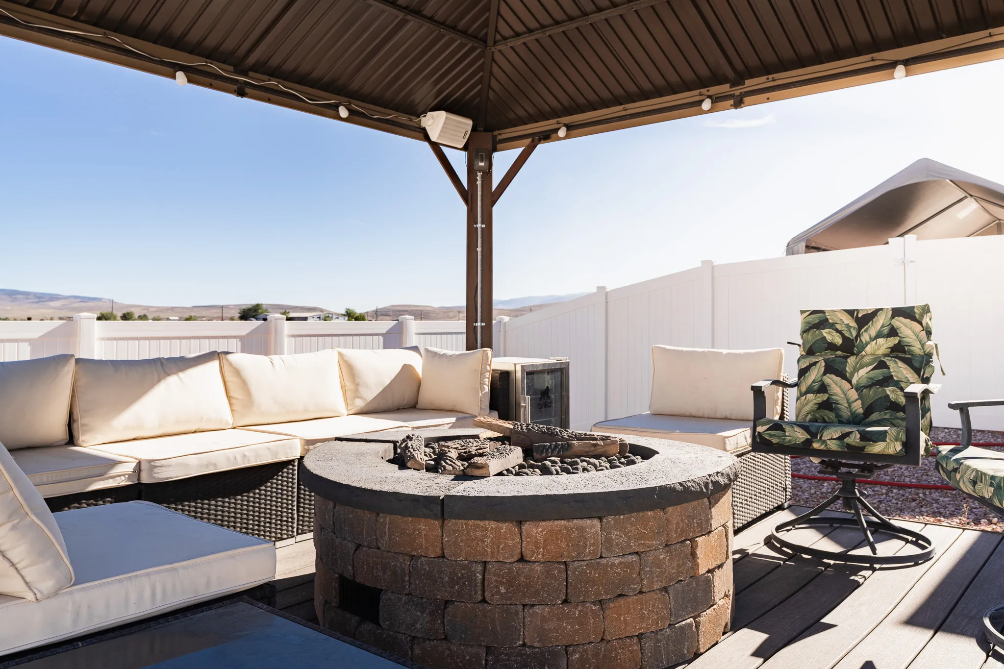 Covered outdoor patio with a composite deck, a built-in stone fire pit, and a white privacy fence