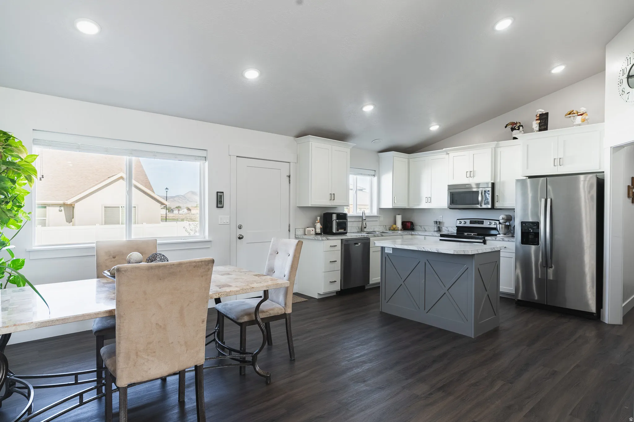 Open-concept living area with vaulted ceilings, recessed lighting, wood-finish flooring, a kitchen island with stone countertop, and stainless steel appliances