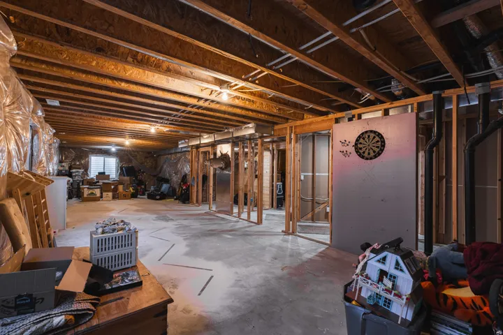 Unfinished basement with exposed wood framing, concrete flooring, and an egress window