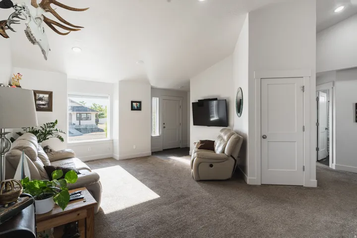 Vaulted ceilings with recessed lighting, large window with natural light, neutral carpeting, white interior doors, and a front entry door with a frosted glass insert