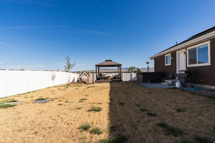 Spacious backyard with a white privacy fence, concrete patio, and a built-in hot tub