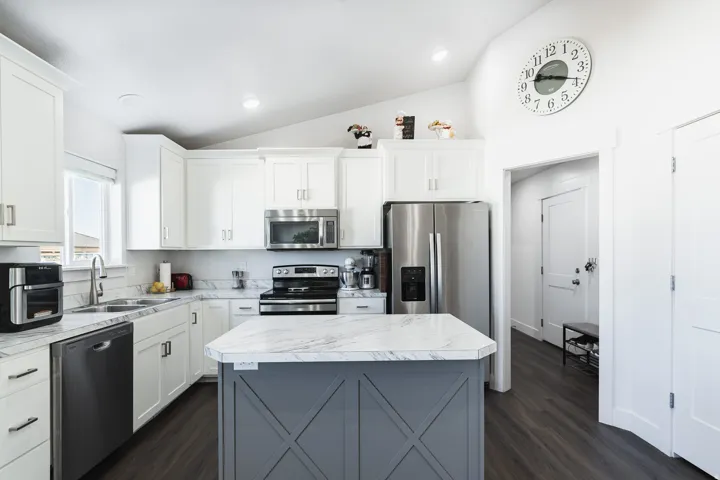 Kitchen featuring white shaker cabinetry, stainless steel appliances, marble-finish countertops, wood-finish flooring, and a central island with a decorative base