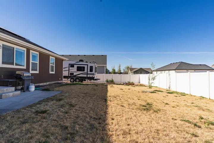 Expansive backyard featuring a concrete patio, privacy fencing, and a gravel strip