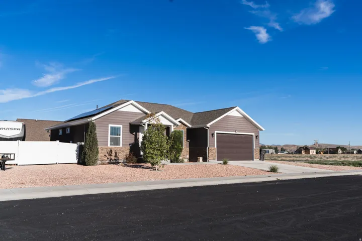 Siding exterior with stone accents, attached garage, solar panels, and a low-maintenance gravel yard