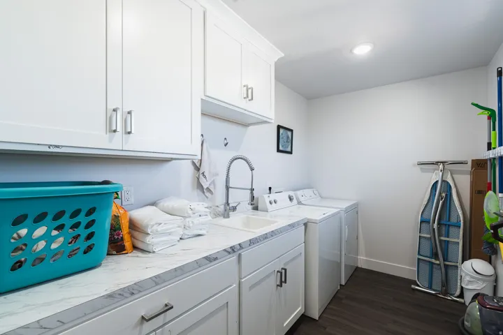 White cabinetry with brushed nickel hardware, laminate countertops, undermount sink with gooseneck faucet, and dark wood-finish flooring
