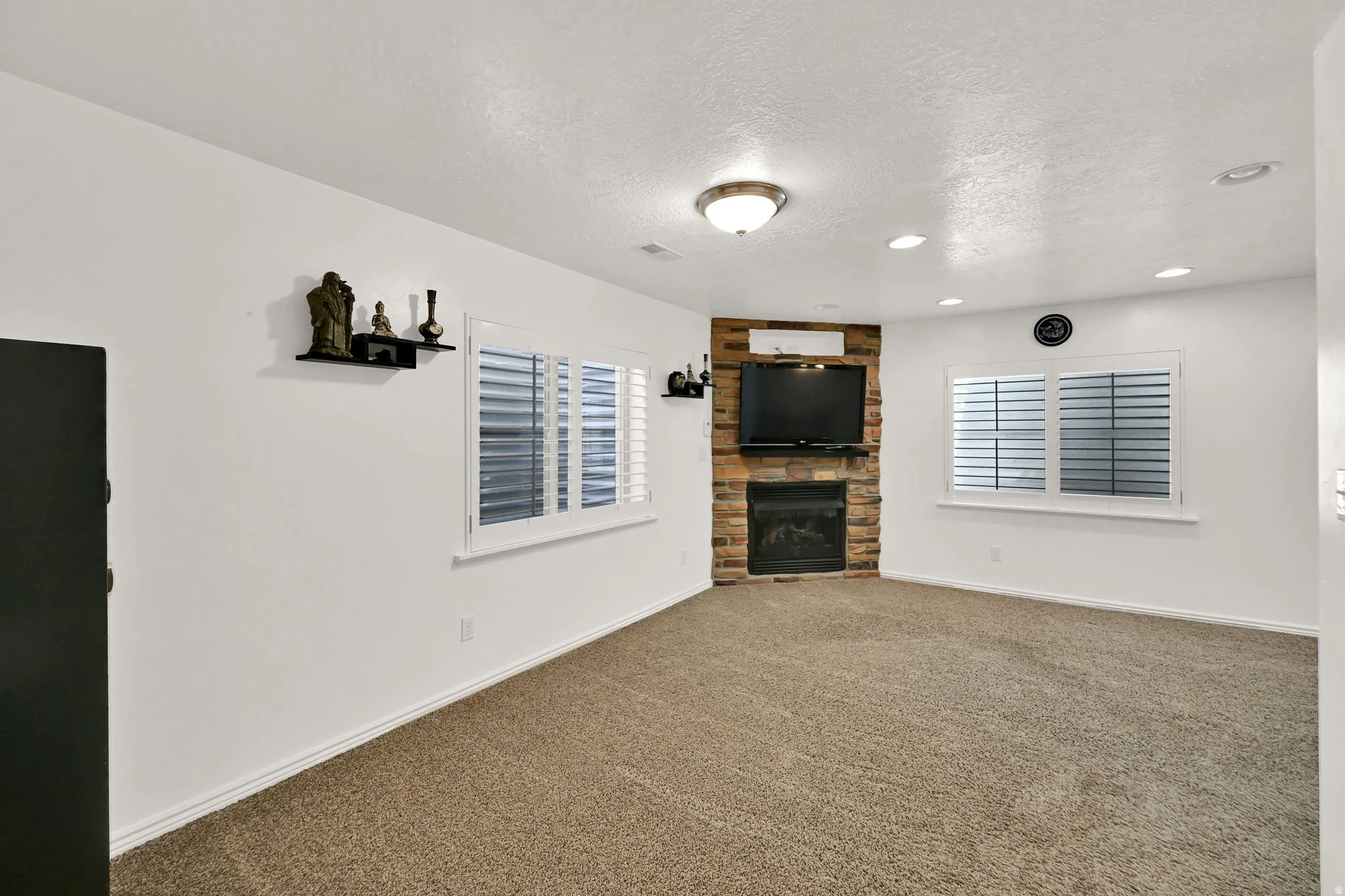 Stone-clad fireplace with a built-in mantel, recessed lighting, and white plantation shutters