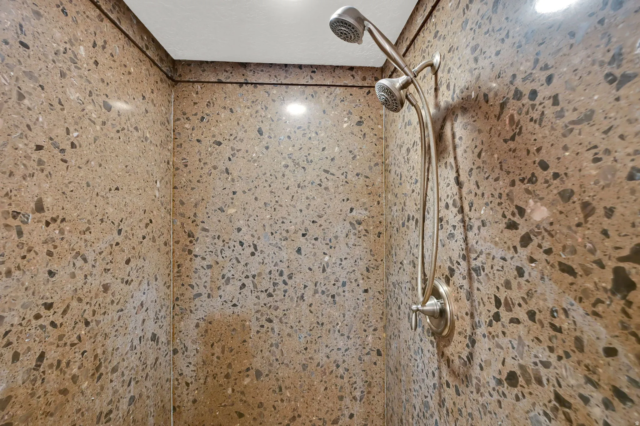 Shower enclosure featuring full-height stone-look wall panels and a brushed metal dual-head shower fixture