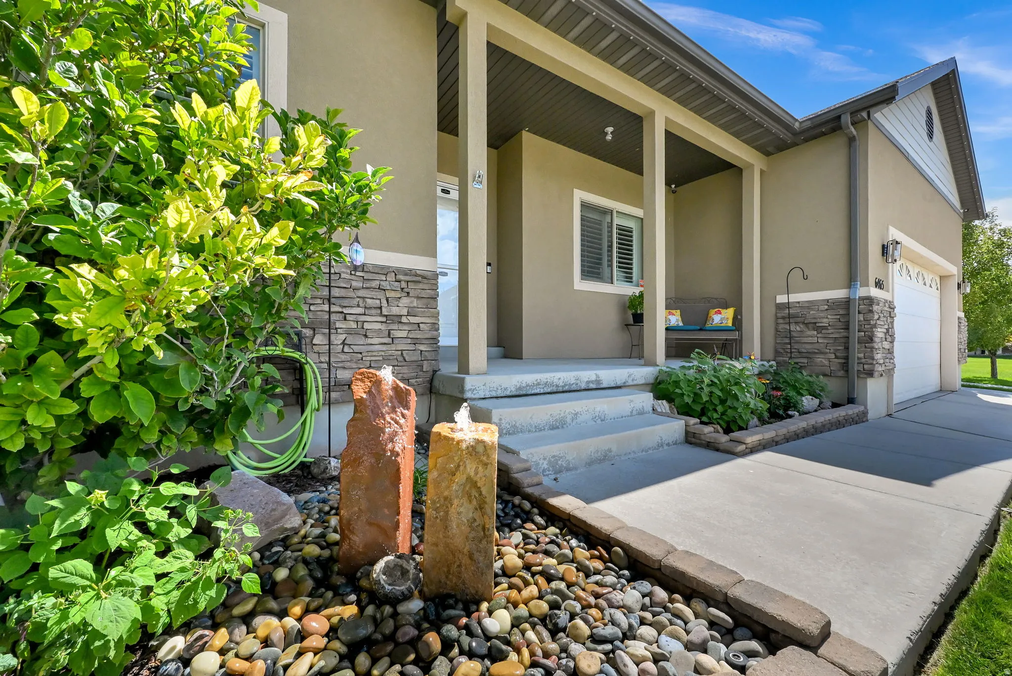 Front exterior with a covered porch, stucco siding, stone accents, and a two-car garage
