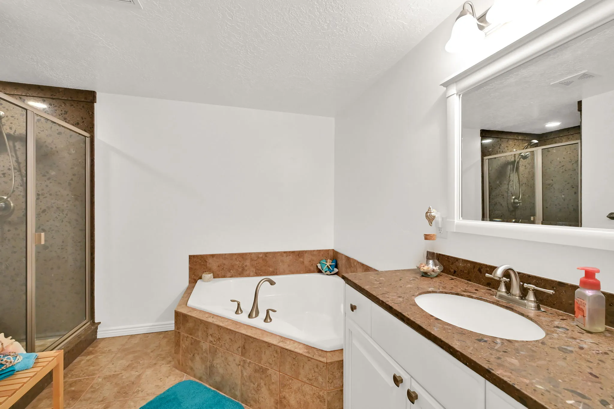 Integrated corner bathtub, walk-in shower with glass enclosure, white vanity cabinet, vanity light fixture, and brown stone-finish countertop
