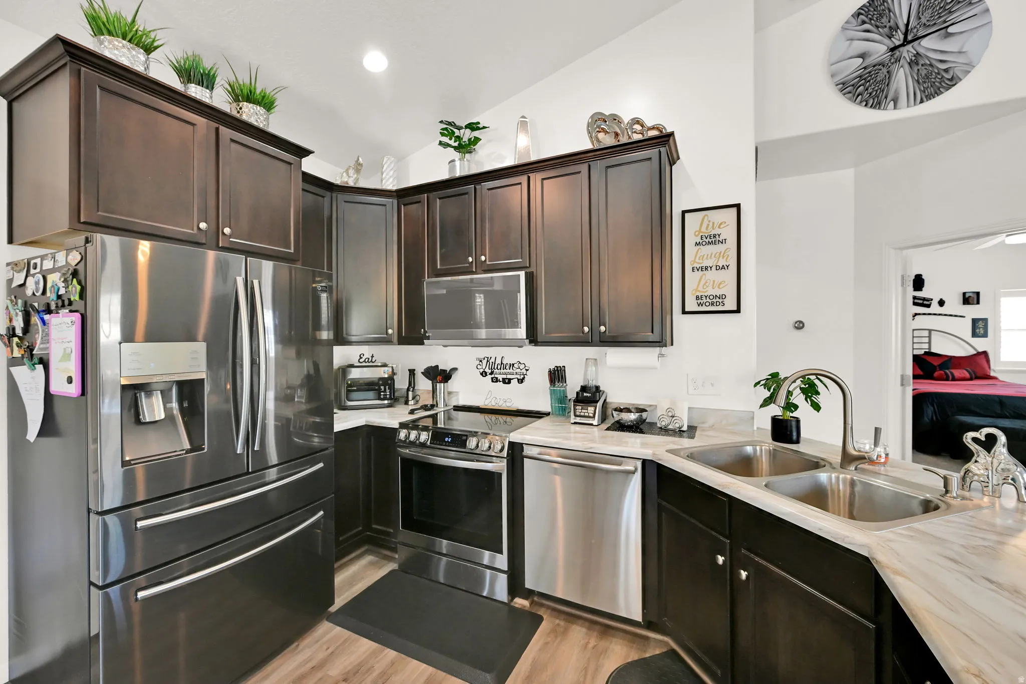 Kitchen featuring dark wood-finish cabinetry, stainless steel appliances, a double basin sink, and light-toned countertops