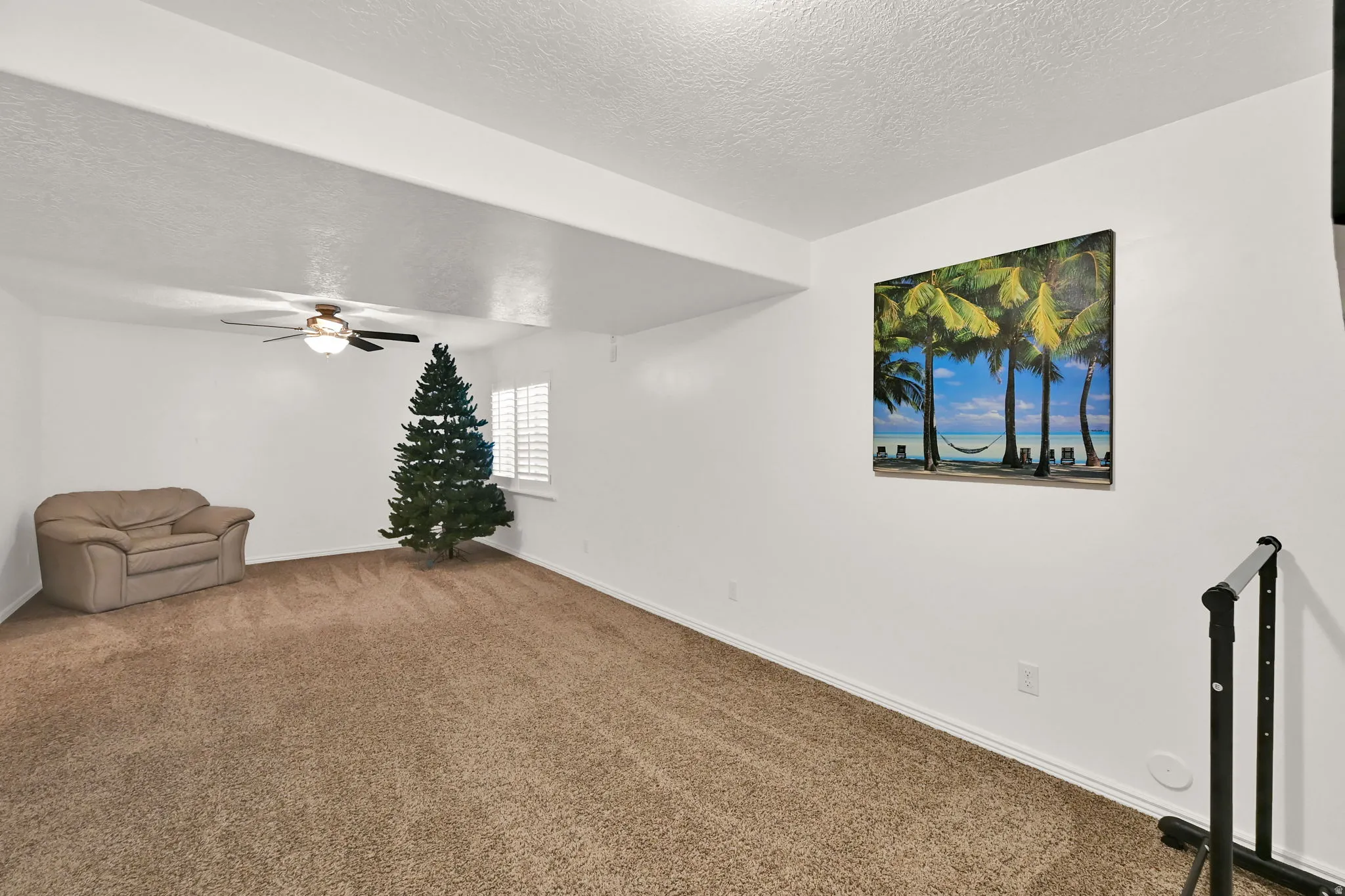 Carpeted interior with white walls, a ceiling fan, and a window with plantation shutters