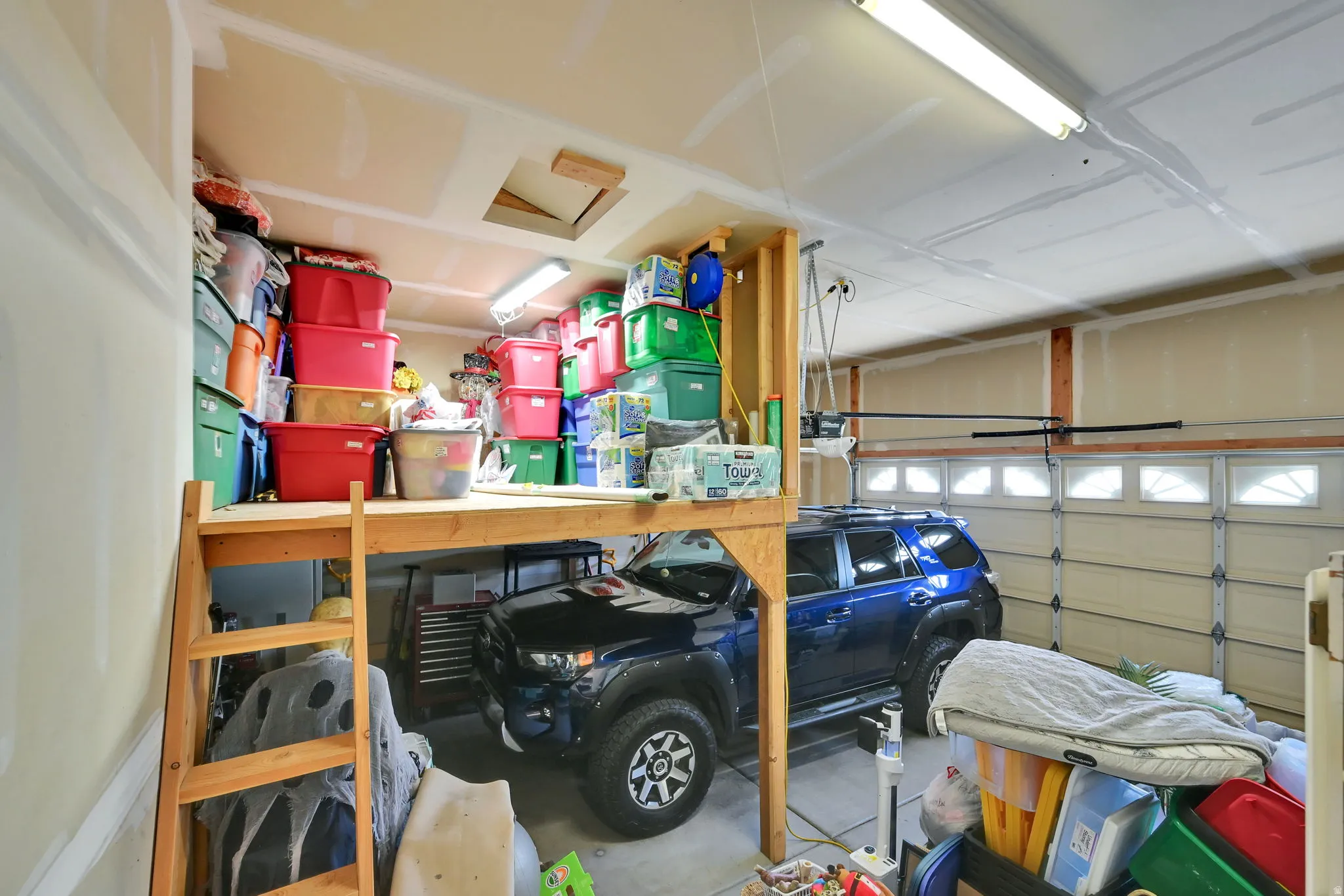 Attached garage with roll-up door, overhead lighting, and built-in wood-frame storage platform
