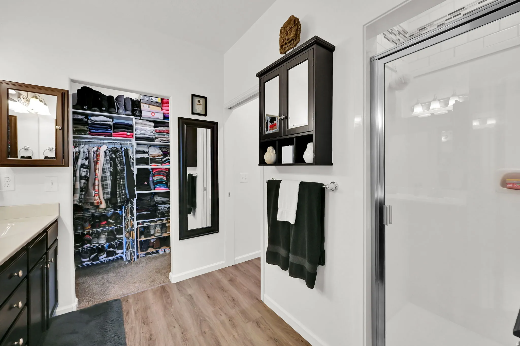 MASTER BATHROOM/WALK-IN CLOSET with built-in shelving, glass-enclosed shower, wall-mounted mirror, wood-finish flooring, and a dark wood-finish vanity
