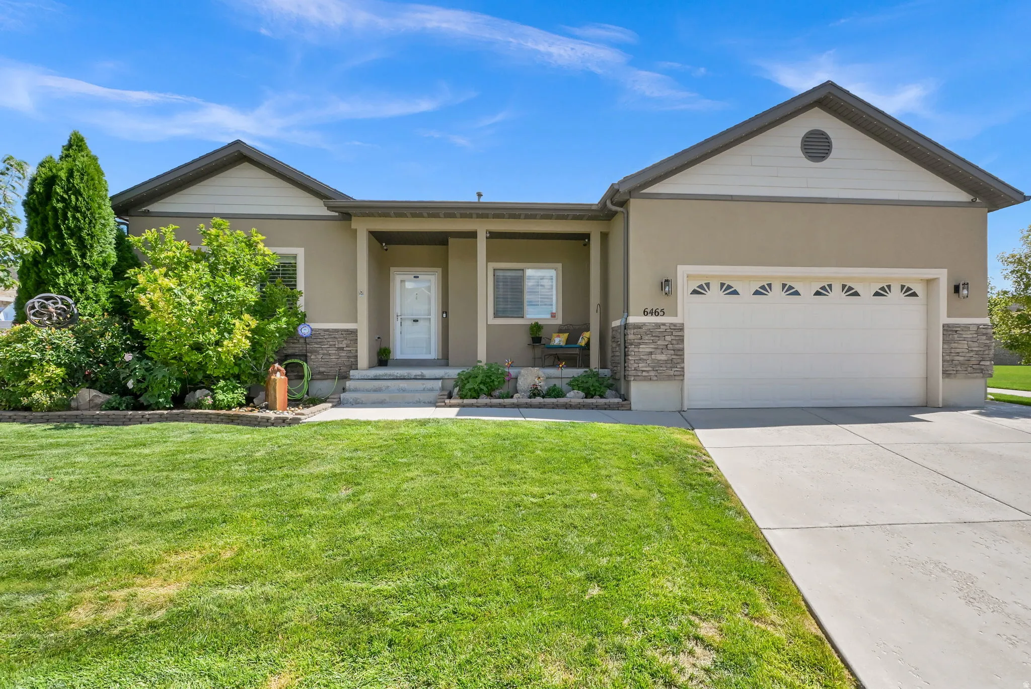 Stucco exterior with stone accents, covered front porch, concrete driveway, attached two-car garage, and established front landscaping