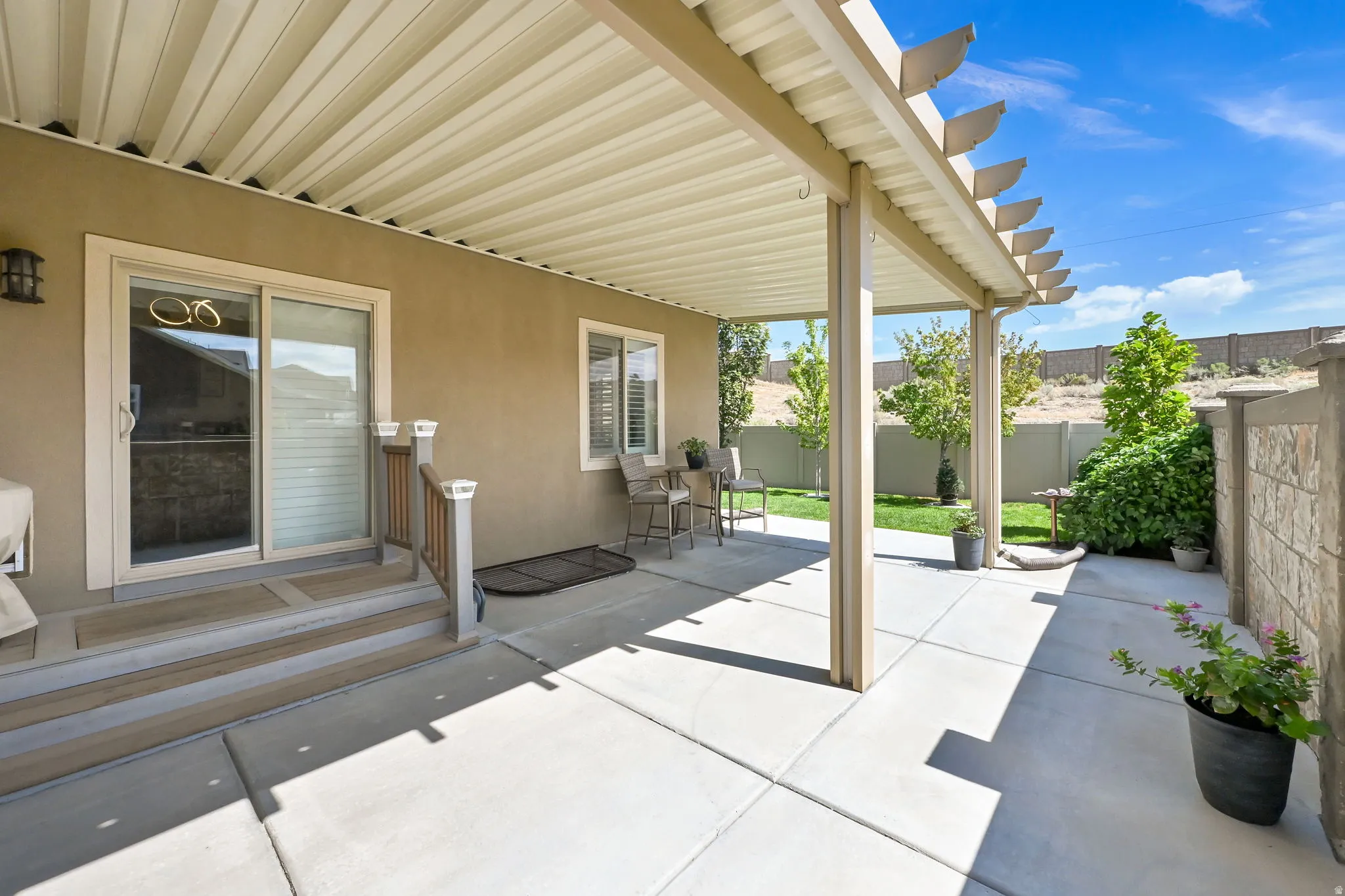 Expansive concrete patio with a covered pergola, stucco exterior, and sliding glass door