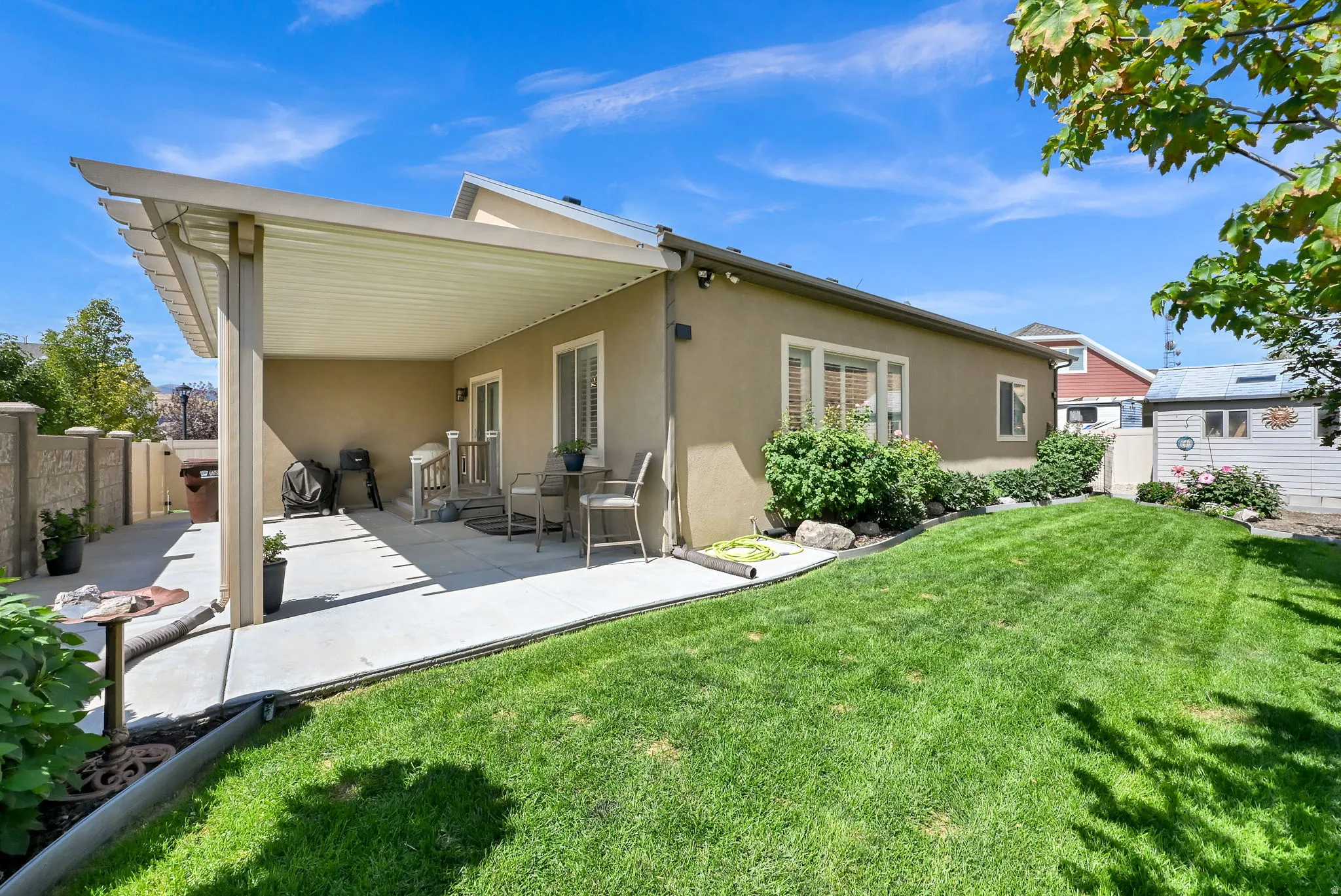 Expansive concrete patio with an attached covered pergola, leading to a vibrant green lawn