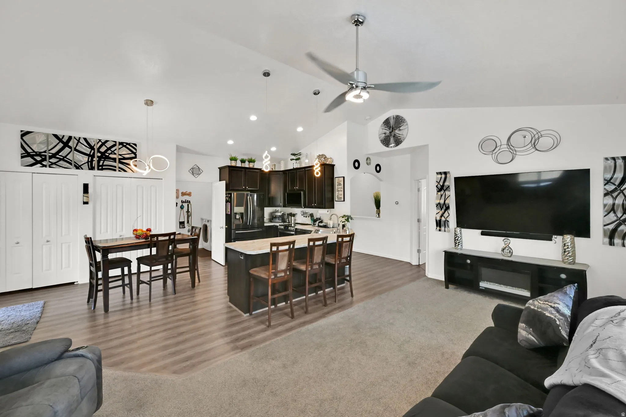 KITCHEN/LIVING ROOM. Vaulted ceilings, wood-finish flooring, dark wood cabinetry, stainless steel appliances, and a kitchen island with seating