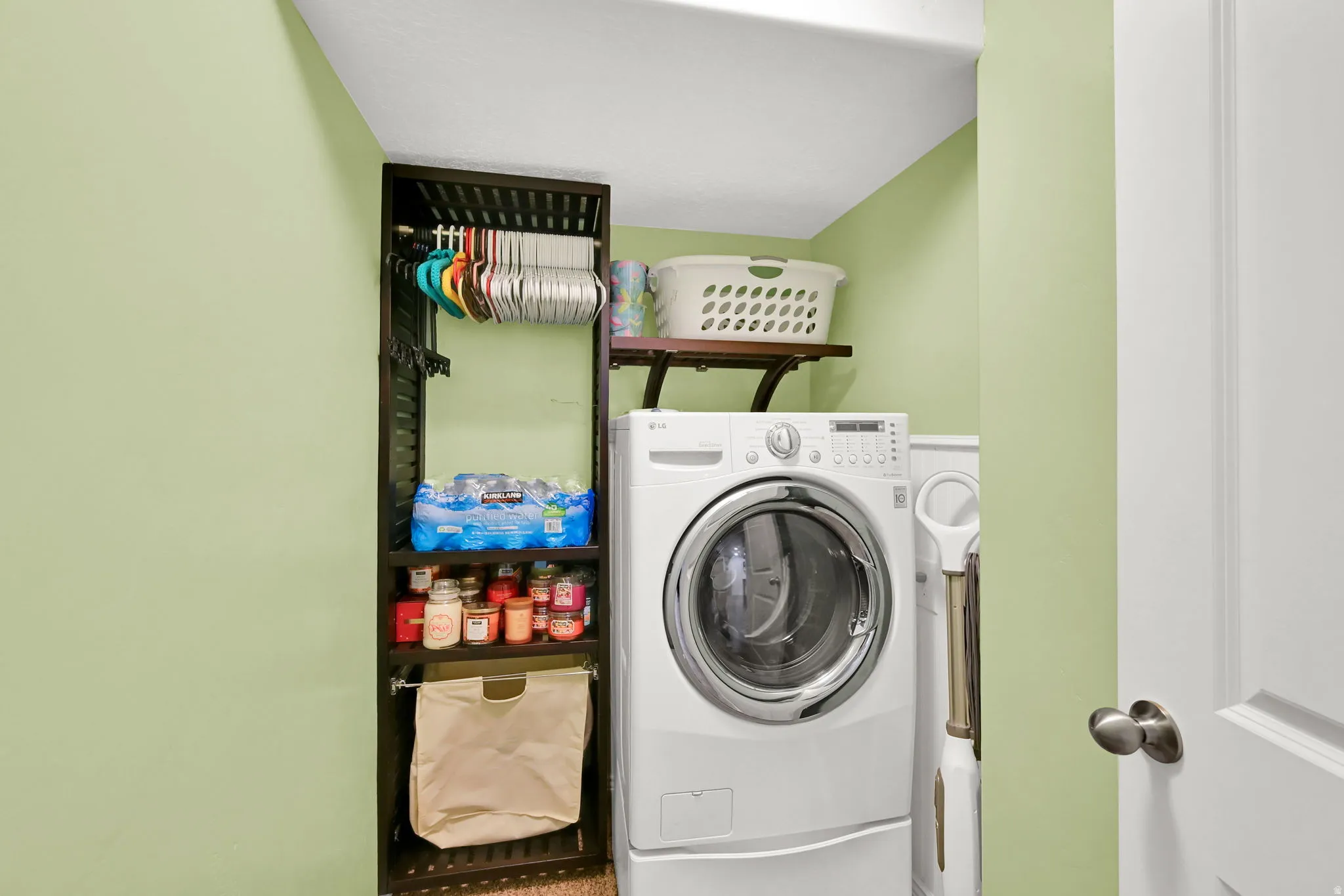Laundry area with a front-loading washing machine, built-in shelving, a wall-mounted shelf, and a white paneled door