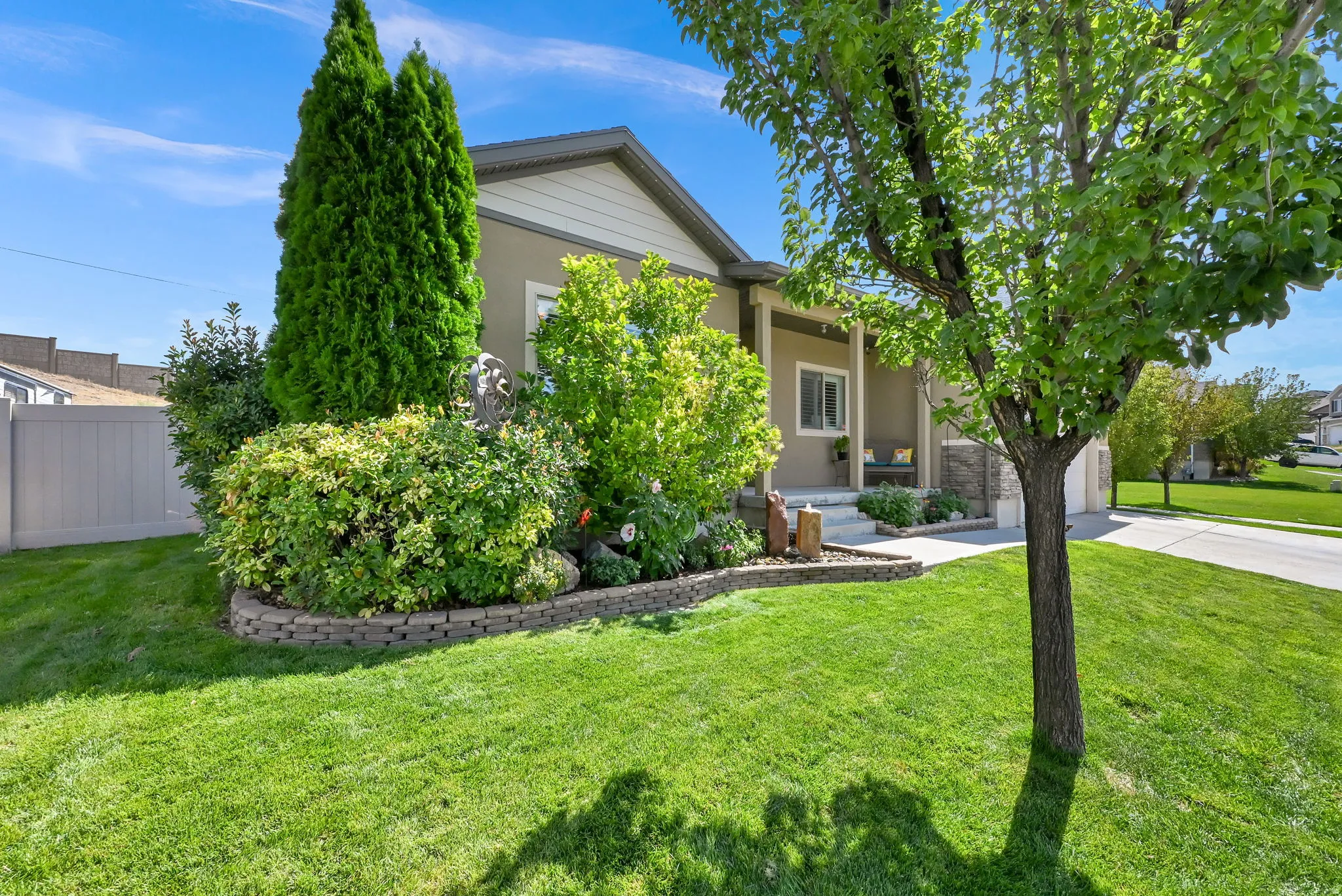 Exterior featuring a covered porch with column supports, stone accents, mature landscaping, a vibrant green lawn, and a paved driveway