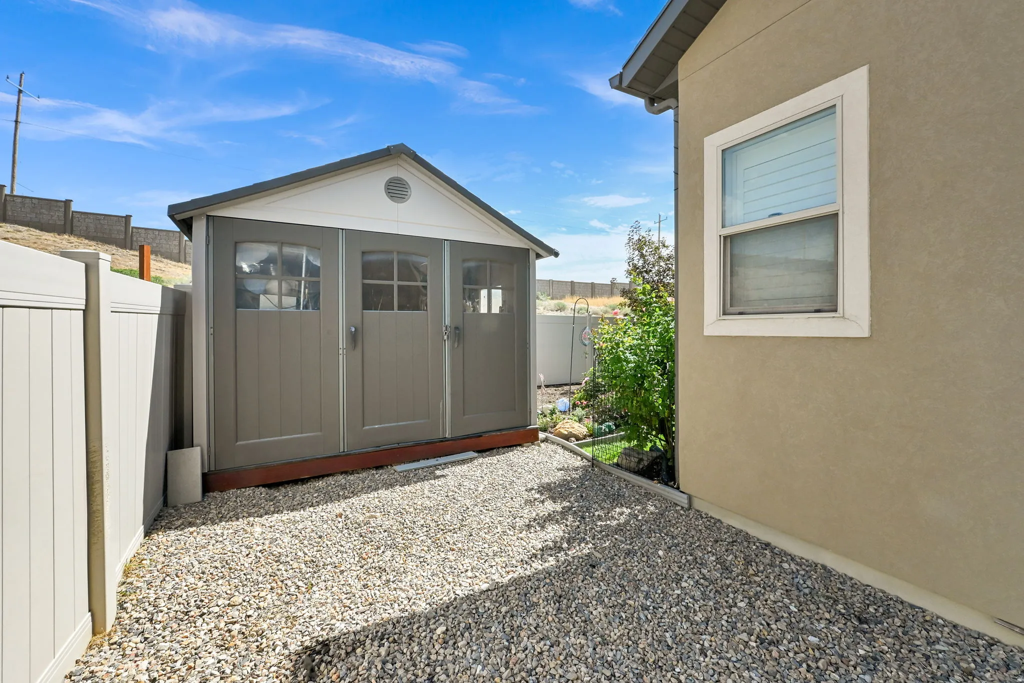 NORTH SIDE OF HOME IN BACKYARD. Gravel-covered side yard featuring a storage shed with double doors and a windowed exterior