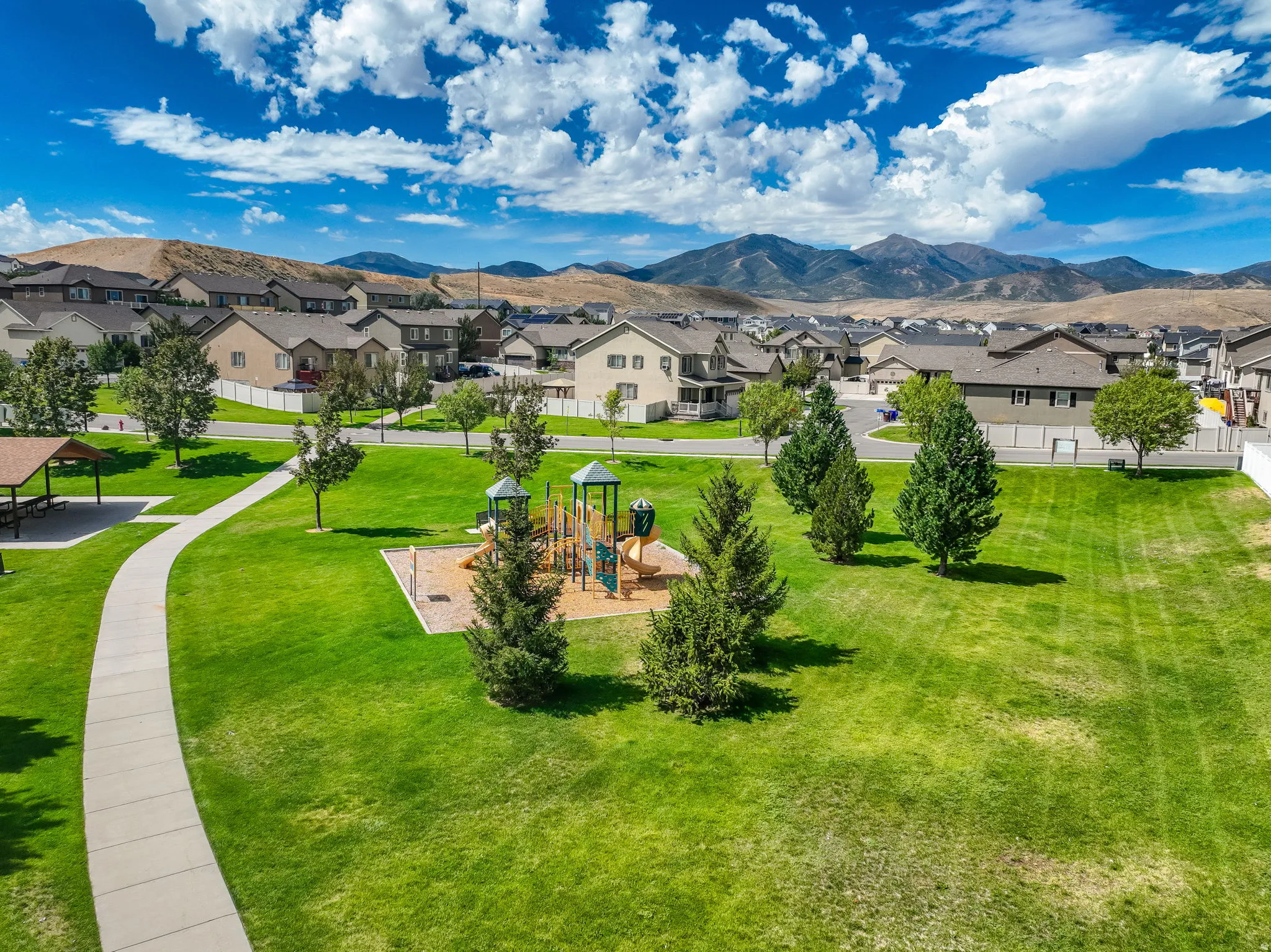 Expansive green space featuring a playground, paved walking paths, and a shaded picnic area