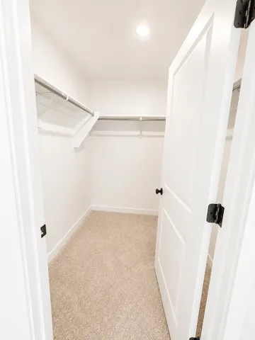 Recessed ceiling light, neutral carpet flooring, white walls, and built-in shelving with hanging rods