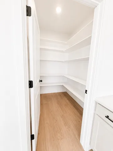 Walk-in pantry featuring extensive white shelving, wood-finish flooring, and recessed ceiling lighting