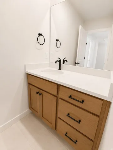 Vanity with wood-finish cabinetry, white countertop, integrated sink, and matte black fixtures
