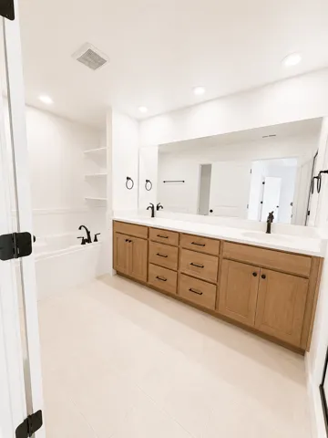 Double vanity with wood-finish cabinetry, white countertop, and black fixtures