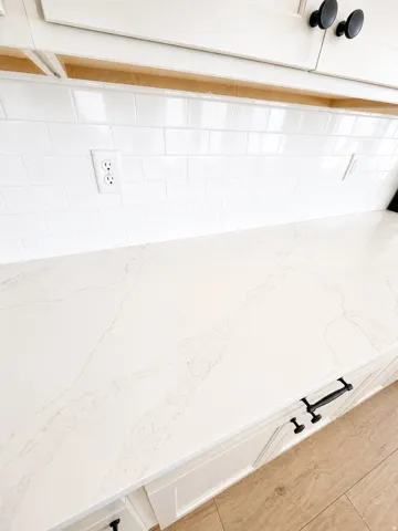 White subway tile backsplash, white cabinetry with black hardware, and wood-finish flooring