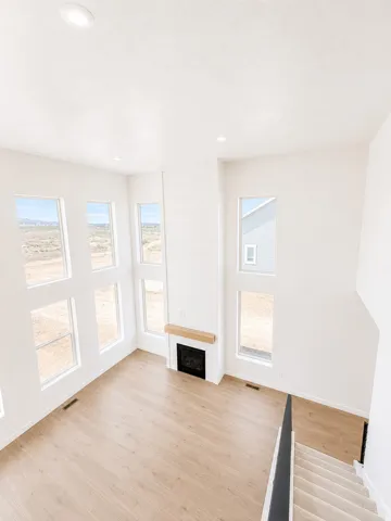 Two-story living area featuring wood-finish flooring, a contemporary fireplace with a wood mantle, recessed lighting, and multiple windows