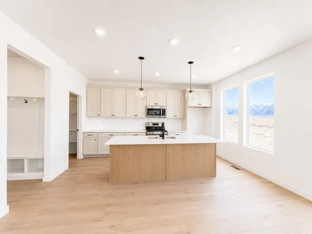 Open-concept kitchen featuring light wood-finish flooring, white cabinetry, a central island with a contrasting wood-finish base, and pendant lighting
