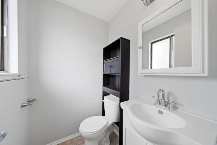 Modern bathroom featuring a curved pedestal sink with chrome faucet, framed mirror with integrated lighting, and a black storage tower with open shelving