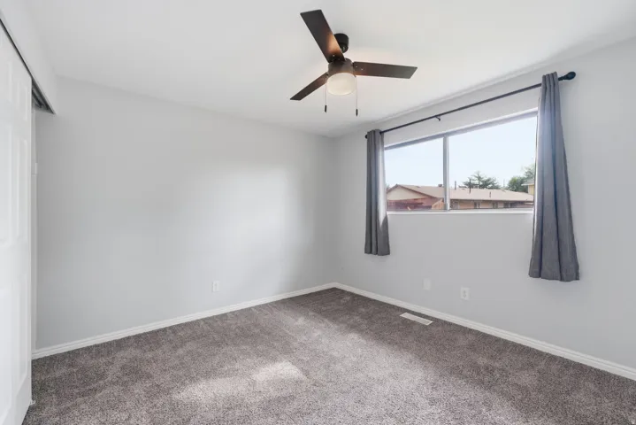 Grey carpeting, neutral wall color, and a ceiling fan with light fixture
