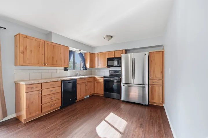 Kitchen featuring wood-finish cabinetry, stainless steel appliances, a white tile backsplash, and wood-finish flooring
