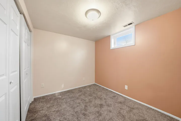 Room featuring textured carpeting, neutral wall finishes, a window, and white bi-fold closet doors