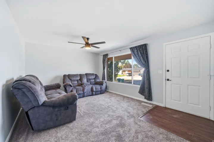 Bright living space featuring a large window, a ceiling fan with integrated lighting, and a paneled entry door