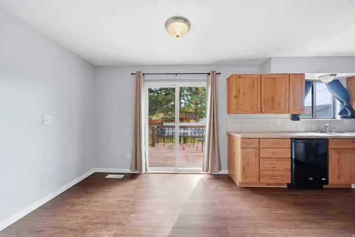 Wood-finish flooring, light wood cabinetry, tiled backsplash, built-in dishwasher, and a sliding glass door to an outdoor deck