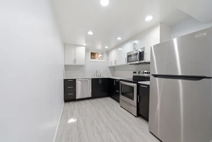 Contemporary kitchen featuring stainless steel appliances, two-tone cabinetry, recessed lighting, and wood-finish flooring